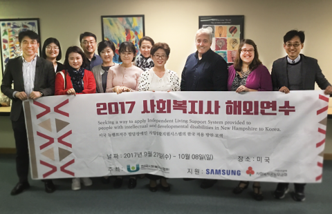 A group of social workers from South Korea and Center for START Services team members holding a banner that reads "Social Work Program Overseas Training" in Korean characters.