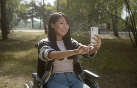 A woman in a wheelchair using her cellphone to video chat with someone