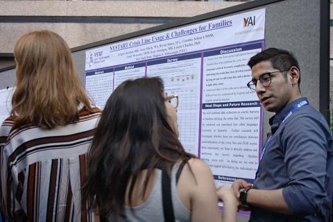 Two people talking in front of a research poster attached to a beige panel