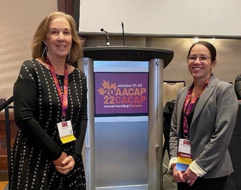 A picture of Jill Hinton and Jennifer McLaren posing in front of a lectern withthe purple and orange conference logo which features a maple leaf.