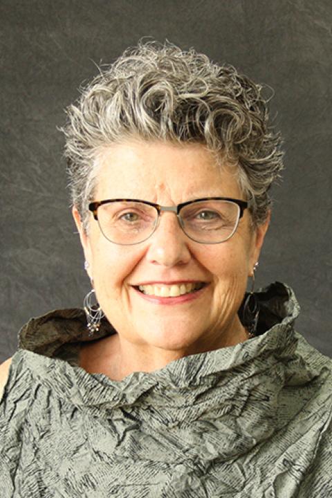 Joan Beasley is a woman with short silver curly stylyed hair and glasses wearing a silver shirt
